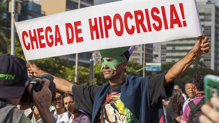 Manifestante segurando uma faixa branca com os dizeres em vermelho "Chega de Hipocrisia!" e usando uma máscara em formato da folha da maconha, durante a Marcha da Maconha RJ 2014.