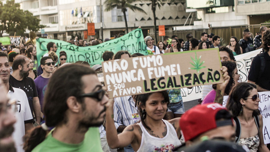 Uma mulher no meio de uma multidão segurando um cartaz com a frase "Não fumo, nunca fumei e sou a favor da legalização". Fumar.