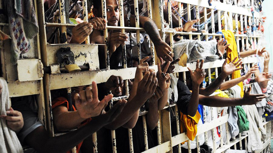 Cela superlotada com dezenas de presos junto às grades com os braços para fora fazendo gestos de paz e liberdade, no Complexo Penitenciário de Pedrinhas, Maranhão. Polícia.