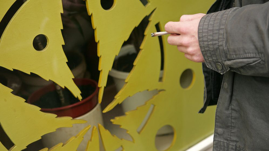 Estrutura amarela vazada com o desenho da folha da maconha e a mão de uma pessoa segurando um baseado. Uruguai.