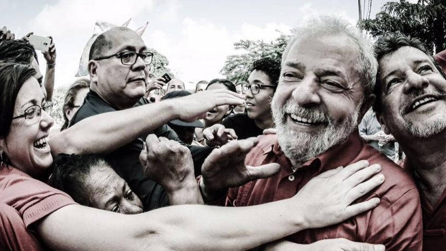 Luiz Inácio Lula da Silva em meio à população que tenta passar pelos seguranças para alcançá-lo.