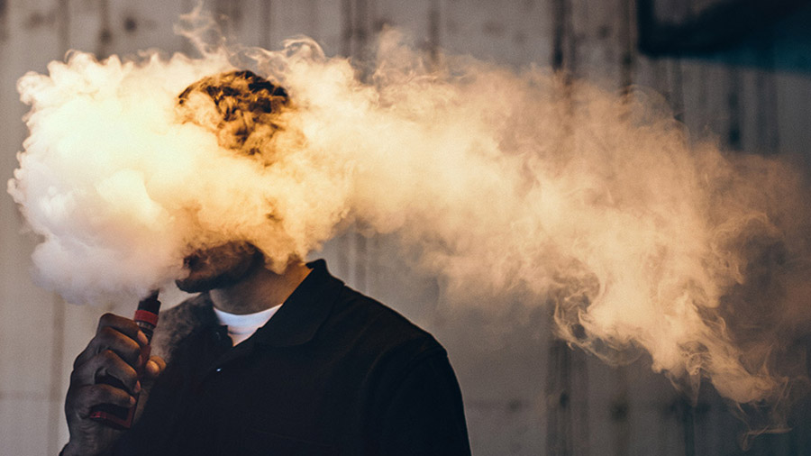 Um homem utilizando um vaporizador envolto em uma nuvem de fumaça. Vaporizar. VapoBoss