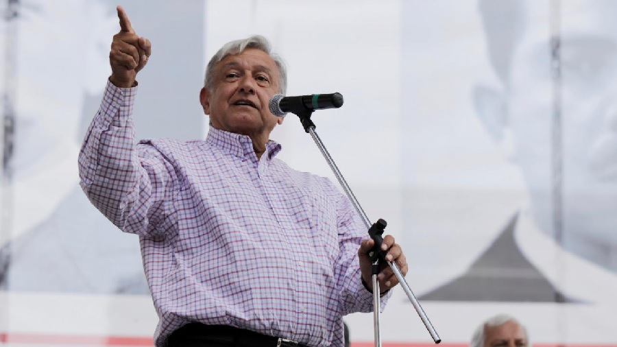 López Obrador em pé, falando ao microfone, segurando o pedestal com uma mão enquanto gesticula com a outra. México.