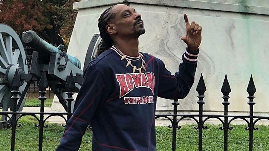 Snoop Dogg gesticulando com uma das mãos e com a cabeça inclinada para cima, e ao fundo o canhão da praça Lafayette.