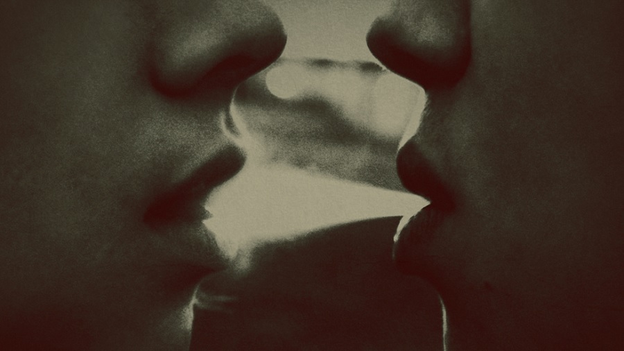 Fotografia em preto e branco que mostra parte do nariz e a boca de duas pessoas, expelindo fumaça de uma boca para a outra.