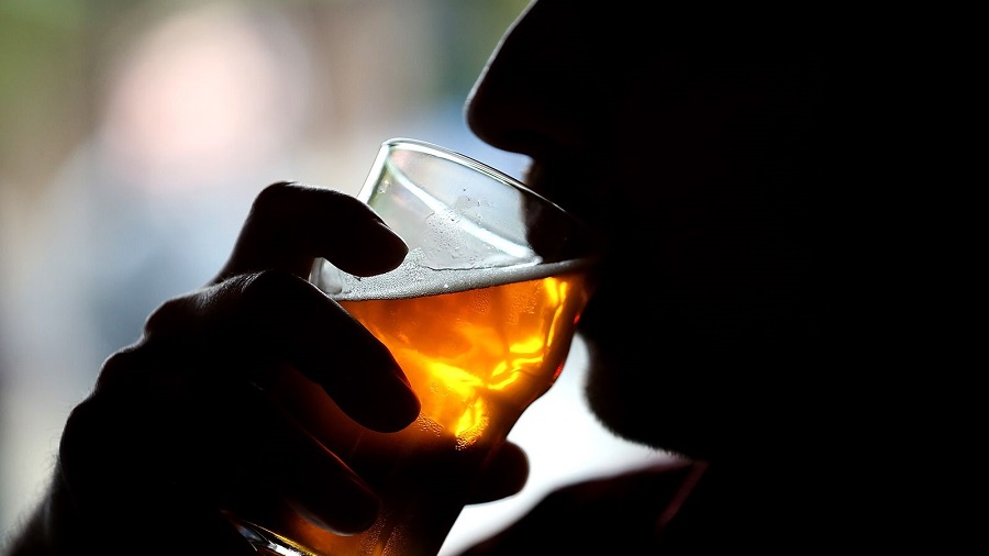 Fotografia mostra a silhueta de uma pessoa em perfil (do nariz ao ombro) que está bebendo um copo de cerveja; e um fundo desfocado. Pesquisa.