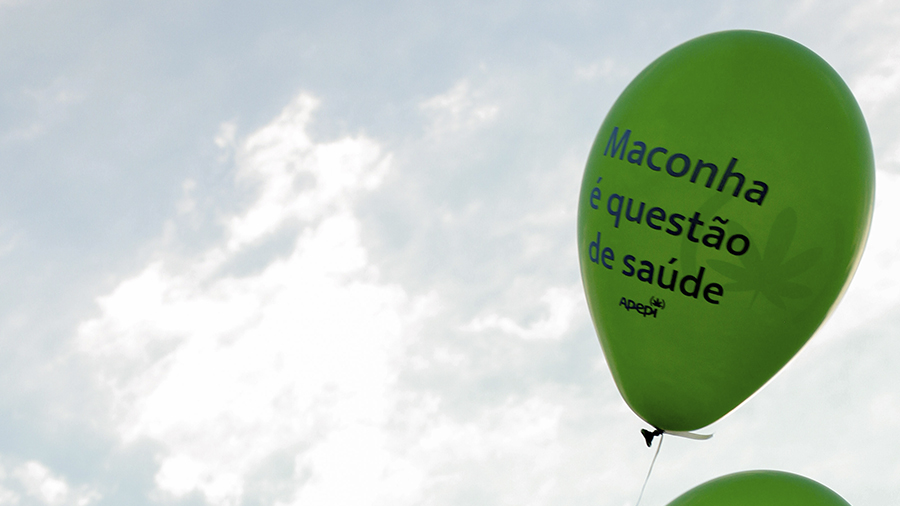 Fotografia que mostra um balão verde com o texto em preto "Maconha é questão de saúde", junto ao logo da Apepi, na parte direita da imagem, e, ao fundo, um céu com nuvens brancas. Foto: Dave Coutinho.
