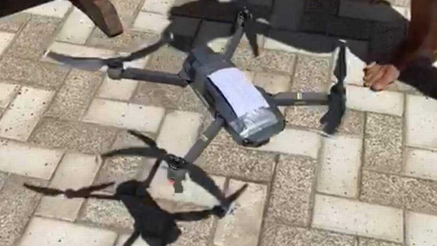 Frame do vídeo que mostra o drone voando próximo ao chão, revestido com lajotas retangulares em tons de bege e marrom-claro.