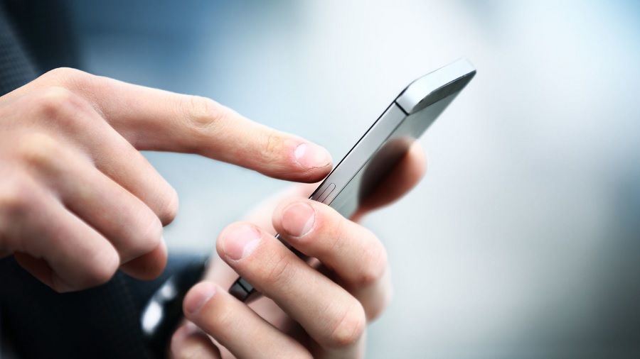 Fotografia em plano fechado que mostra as mãos de uma pessoa mexendo em um celular e um fundo em tons de azul e cinza. Foto: Jeso Carneiro | Flickr.