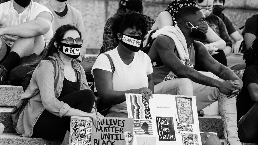 Fotografia, em preto e branco e vista diagonal, que mostra diversas pessoas sentadas em uma escadaria, usando máscaras e segurando cartazes, em vigília por justiça e George Floyd. Imagem: Victoria Pickering | Flickr.