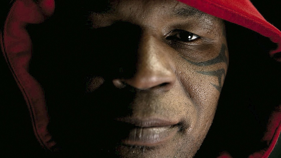 Foto de rosto de Mike Tyson, com um capuz vermelho e a luz incidindo da direita, deixando o outro lado de sua face com sombra. Imagem: MSRK TV | Vimeo.