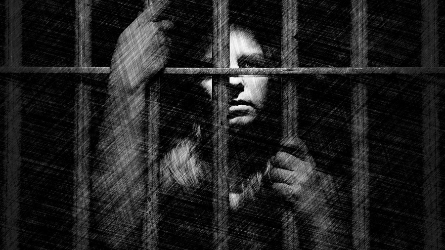 Ilustração em preto e branco de uma mulher atrás das grades de uma cela, que segura com as duas mãos, onde sua face contrasta com o fundo escuro. Imagem: Sarayuth Pinthong | Força Aérea dos EUA.