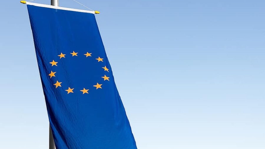 Fotografia que mostra a bandeira europeia hasteada na vertical, na parte esquerda da imagem, e um céu limpo ao fundo. Foto: Pikist.