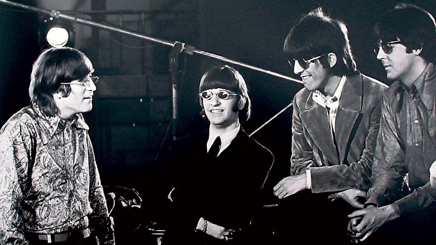 Fotografia em preto e branco dos Beatles, que mostra John Lennon e George Harrison, este com óculos escuros e paletó preto, enquanto o primeiro olha para Ringo e Paul que estão sentados, na parte direita da foto, que é a contracapa de Revolver.