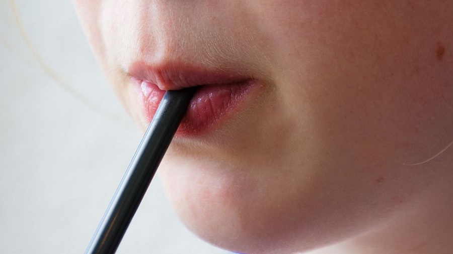 Fotografia que mostra, em meio perfil, a boca de uma pessoa sugando em um canudo de cor preta que contrasta com o fundo braço, na parte esquerda da imagem. Foto: Anemone123 | Pixabay.