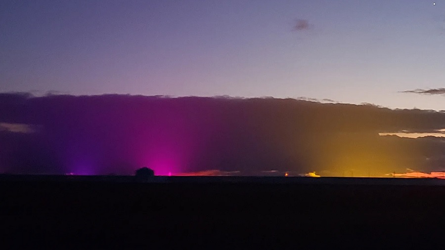 Fotografia registrada em Leamington, no início da noite, que mostra o céu com nuvens iluminadas por luzes de cor roxa, rosa e amarela e dividindo uma linha reta com o horizonte escuro. Foto: Peter Loewen | The Detroit News.