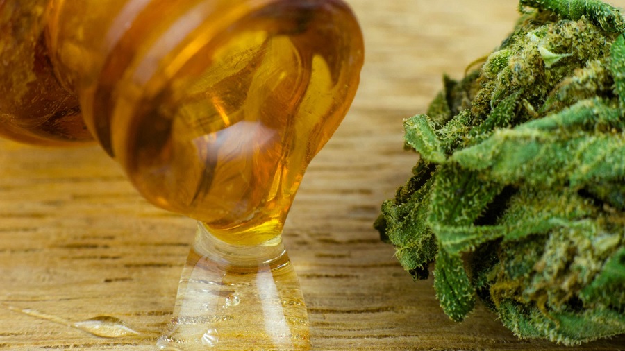 Fotografia que mostra a boca de um frasco cor âmbar vertendo um gel translúcido sobre uma superfície de madeira clara, onde também se vê um bud de cannabis. Foto: High Times.