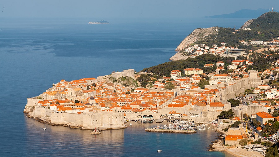 Fotografia aérea que mostra a cidade de Dubrovnik, uma península cercada por grandes muralhas e repleta de casas e construções, na Croácia. Imagem: Diego Delso | Wikimedia Commons.