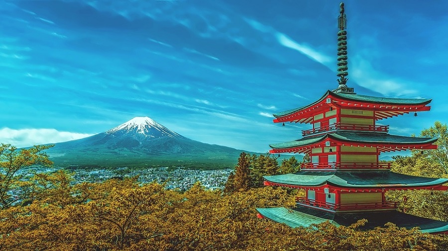 Fotografia que mostra o Monte Fuji (Japão) e parte da cidade de Fujiyoshida, ao fundo, na parte esquerda da imagem, e, no primeiro plano, o templo Pagode Chureito cercado de cerejeiras com folhas de cor castanho-acobreado; um céu azul com poucas nuvens completa o quadro. Foto: Walkerssk | Pixabay.