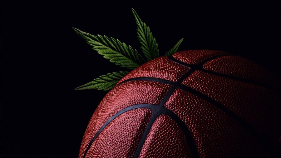 Fotografia que mostra parte de uma bola de basquete e uma folha de maconha que aparece atrás da mesma, em fundo escuro.