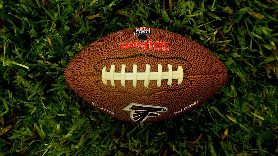Foto tirada de cima pra baixo de uma bola de futebol americano do Atlanta Falcons, na horizontal, em um gramado. Imagem: Lernestorod | Pixabay.