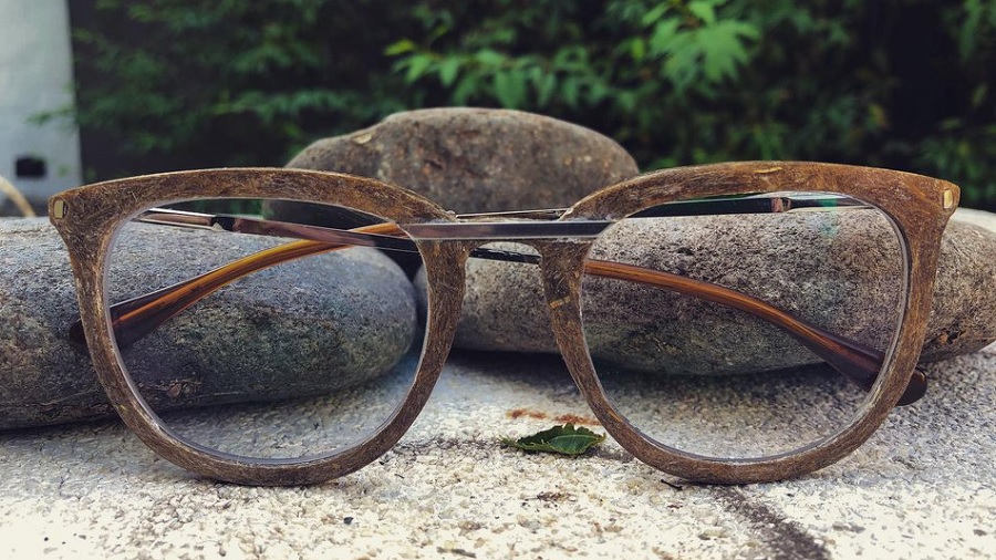 Foto dos óculos de cânhamo sobre uma rocha e apoiados em outras duas, e uma sebe viva ao fundo. Crédito: divulgação / Gaia Eyewear.