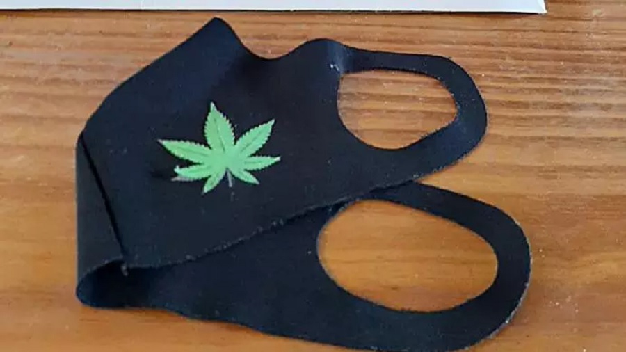 Fotografia que mostra uma máscara de tecido preta com o desenho de uma folha de maconha estampado sobre uma superfície de madeira. Foto: PMMG.