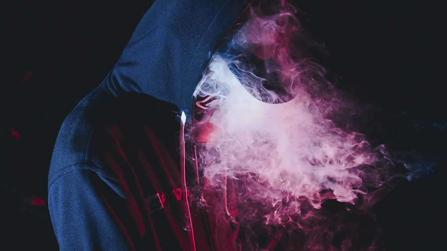 #PraCegoVer: Em destaque, fotografia de uma pessoa de lado, vestindo capuz e boné com o rosto envolto de fumaça. Foto: Wild Vibes|Unsplash vapes