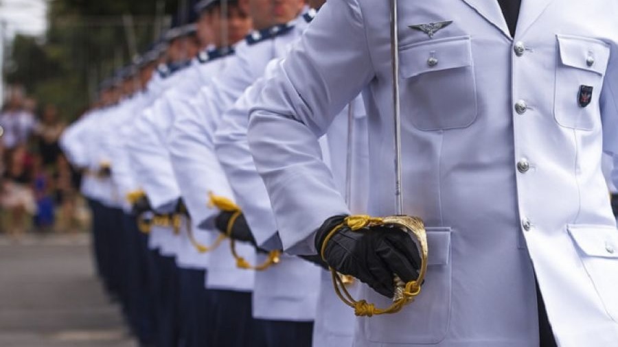 Fotografia mostra, em vista diagonal, uma fileira de oficiais da FAB usando túnica branca e calça azul e segurando a espada alinhada junto ao corpo. Foto: Agência Força Aérea.