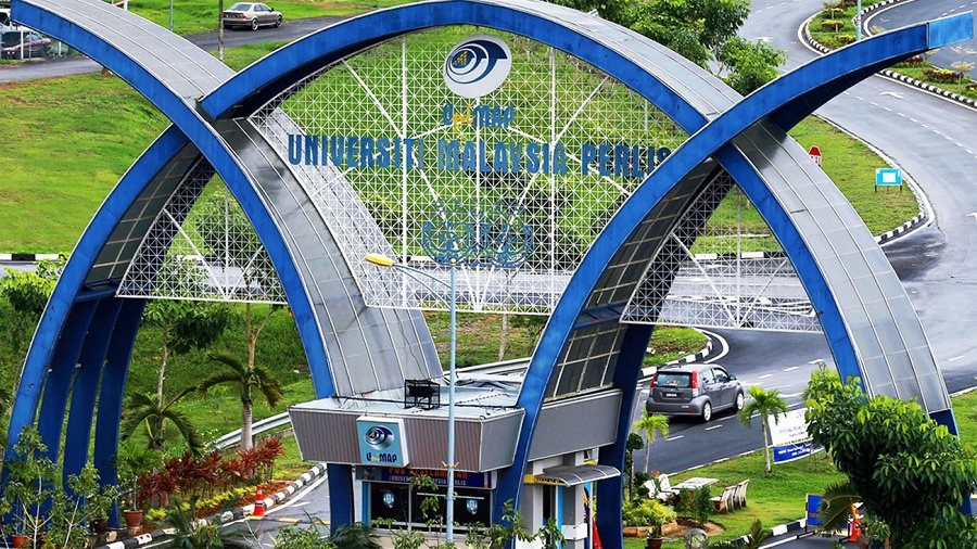Fotografia aérea mostra a entrada do campus da Universidade Malásia Perlis, onde uma estrutura de arcos azuis que se interseccionam abriga a portaria de carros, adjacente a uma área com árvores e gramado. Foto: divulgação.