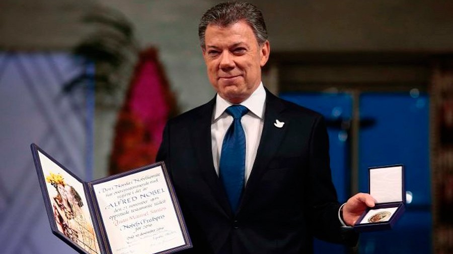 Fotografia mostra Juan Manuel Santos, vestido com paletó preto e gravata azul, segurando o diploma e a medalha do prêmio Nobel da Paz. Foto: Håkon Mosvold Larsen / NTB.