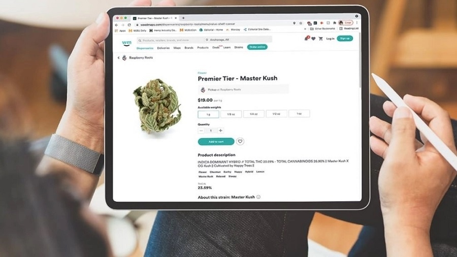 Fotografia mostra a tela de um tablet que exibe uma opção de cannabis vendida na plataforma da Weedmaps e as mãos da pessoa que o segura apoiado sobre a perna. Imagem: MJBizDaily.