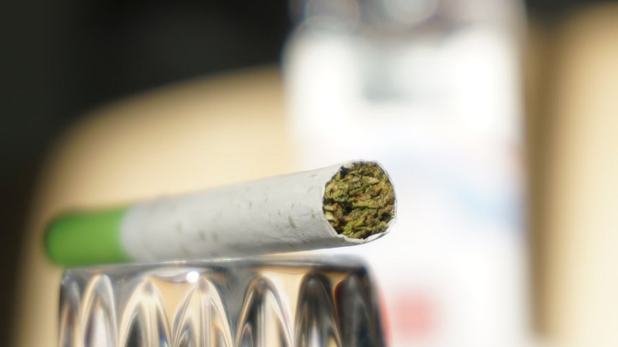 Fotografia de um cigarro industrializado de delta-8-THC com filtro verde, em perspectiva, sobre um objeto de vidro, em fundo embaçado. Imagem: Unsplash | Elsa Olofsson.