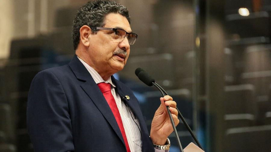 Foto, em meio perfil, do deputado João Paulo, que, usando paletó cinza-escuro e gravata vermelha, segura o microfone da tribuna, em fundo embaçado. Imagem: Alepe.