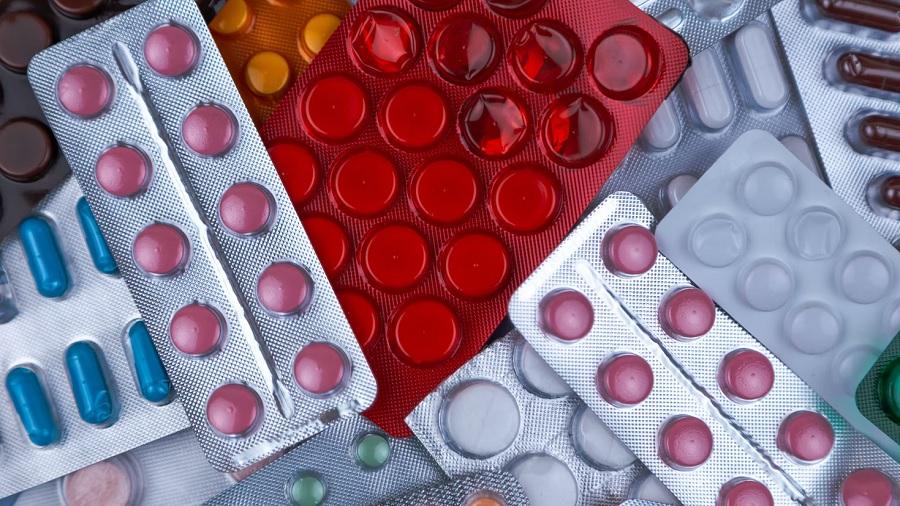 Foto, em vista superior, mostra várias cartelas de medicamentos, sendo uma vermelha, contendo comprimidos de várias cores e formatos. Imagem: Unsplash / Volodymyr Hryshchenko.