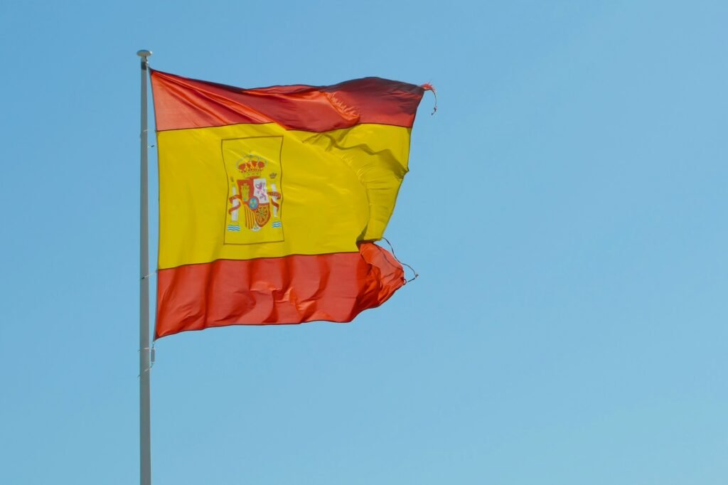 Fotografia mostra bandeira da Espanha flanando em fundo de céu azul Foto layo animals unsplash