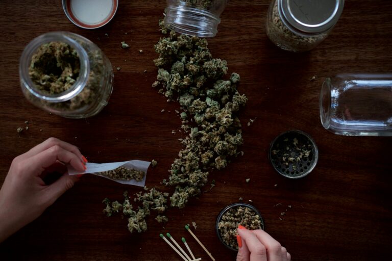 Imagem aérea de uma mesa com uma porção de cannabis e duas mãos femininas manipulando o produto Foto Wesley Gibbs Unsplash. advogado.