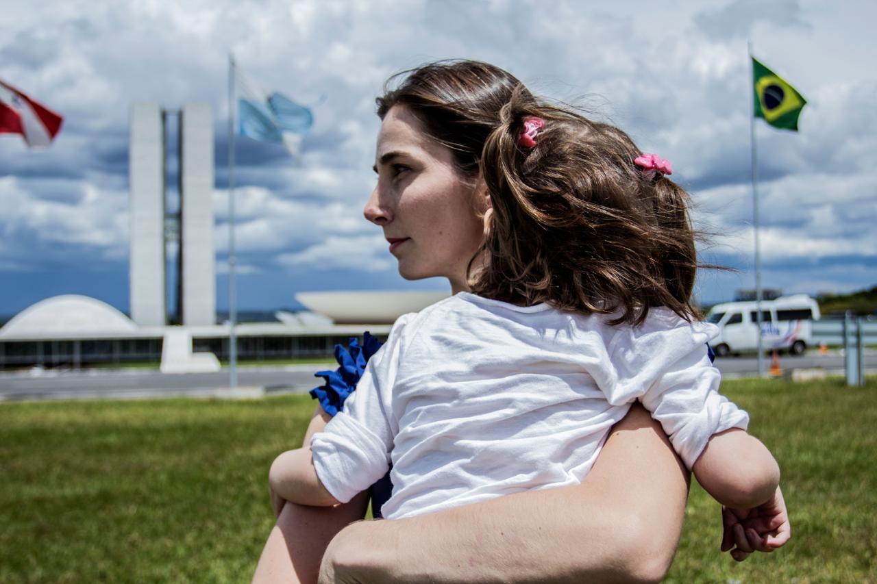 Katiele Fisher com sua filha no colo e o congresso nacional ao fundo. Cena do filme Ilegal. Crédito: divulgação. filmes.