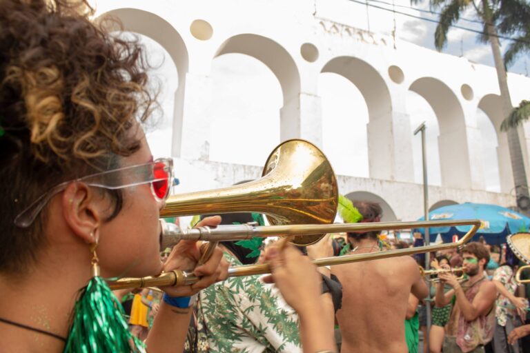 Fotografia mostra uma mulher tocando trombone no desfile do Bloco Planta na Mente, na Lapa (Rio de Janeiro). Foto: Dave Coutinho.